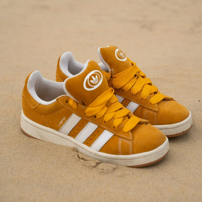 Pair of mustard yellow adidas sneakers on sand.